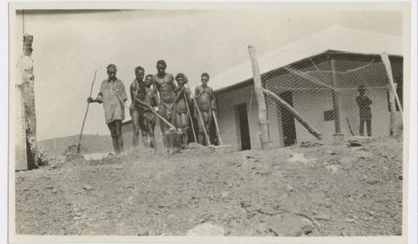 Six Aboriginal men in chains with tools in front of a Halls Creek Hospital  (Photo: M.E. McCombe 'nursing days')